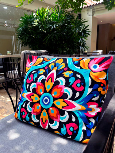 Colorful patterned pillow on a chair outdoors with plants and furniture in the background